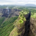 A dramatic view of Sandhan Valley in Maharashtra, showcasing towering rock walls, a narrow gorge pathway, and scattered boulders under natural daylight.