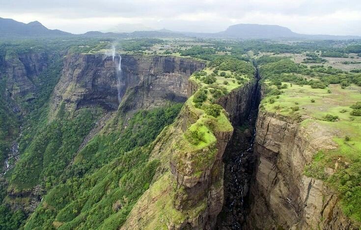 A dramatic view of Sandhan Valley in Maharashtra, showcasing towering rock walls, a narrow gorge pathway, and scattered boulders under natural daylight.