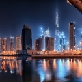 Nighttime view of Business Bay in Dubai, showcasing illuminated skyscrapers, modern architecture, and vibrant city lights reflecting on the water.