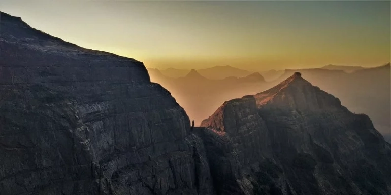 Harishchandragad Fort in Maharashtra featuring rugged cliffs, ancient caves, and the iconic Konkan Kada viewpoint surrounded by misty mountains and lush greenery.