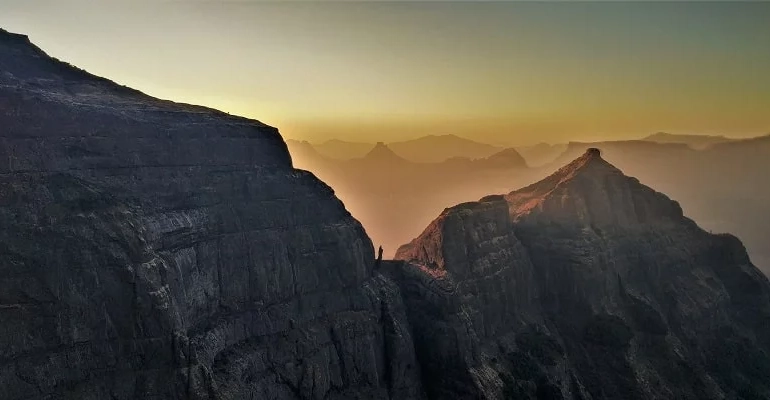 Harishchandragad Fort in Maharashtra featuring rugged cliffs, ancient caves, and the iconic Konkan Kada viewpoint surrounded by misty mountains and lush greenery.