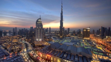 Panoramic view of Downtown Dubai featuring the Burj Khalifa, luxury hotels, modern skyscrapers, and the bustling cityscape under a clear blue sky.