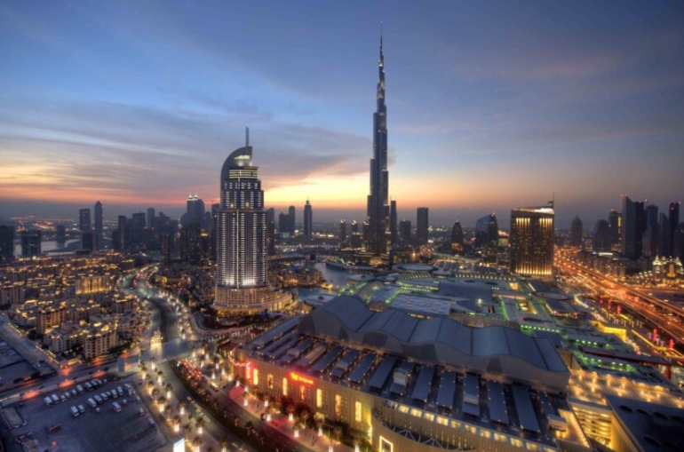 Panoramic view of Downtown Dubai featuring the Burj Khalifa, luxury hotels, modern skyscrapers, and the bustling cityscape under a clear blue sky.