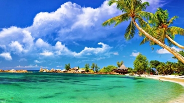 A panoramic view of the coastal city of Port Blair featuring turquoise waters, green hills, and scattered buildings along the shoreline under a partly cloudy sky.