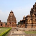 Historic Chalukyan temple complex made of intricately carved reddish-brown stone, with tall spires and sculptures, set against a dramatic cloudy sky in Pattadakal, Karnataka.