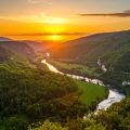Scenic sunset over a lush green valley in Dandeli with a winding river flowing between forest-covered hills, creating a tranquil and picturesque landscape.
