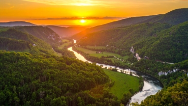 Scenic sunset over a lush green valley in Dandeli with a winding river flowing between forest-covered hills, creating a tranquil and picturesque landscape.