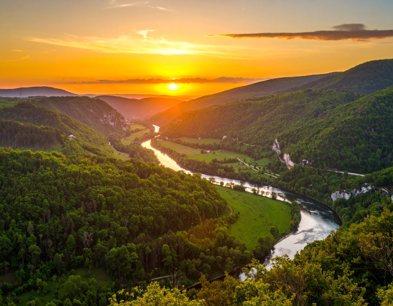 Scenic sunset over a lush green valley in Dandeli with a winding river flowing between forest-covered hills, creating a tranquil and picturesque landscape.