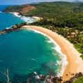 A stunning aerial shot of Gokarna's crescent-shaped beach in Karnataka, India, showcasing golden sands, lush green hills, and the clear waters of the Arabian Sea ideal for nature lovers and beachgoers.