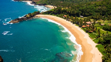 A stunning aerial shot of Gokarna's crescent-shaped beach in Karnataka, India, showcasing golden sands, lush green hills, and the clear waters of the Arabian Sea ideal for nature lovers and beachgoers.
