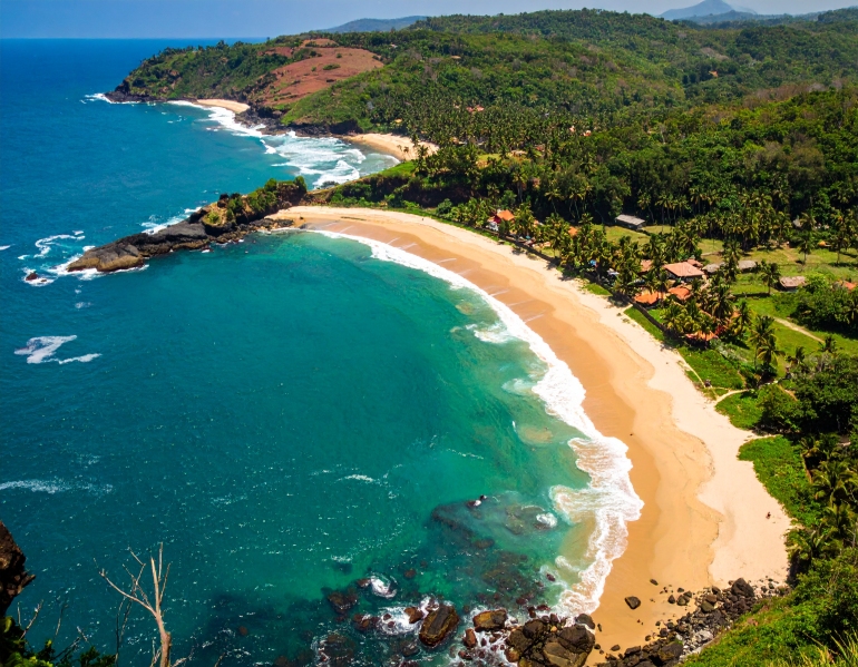 A stunning aerial shot of Gokarna's crescent-shaped beach in Karnataka, India, showcasing golden sands, lush green hills, and the clear waters of the Arabian Sea ideal for nature lovers and beachgoers.
