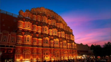 The iconic Hawa Mahal in Jaipur, Rajasthan, showcasing its unique pink sandstone honeycomb façade with numerous small windows and intricate latticework under a clear sky.