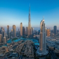 A majestic view of the Burj Khalifa in Dubai, soaring into a clear blue sky, surrounded by modern skyscrapers and urban landscape in the foreground.