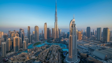 A majestic view of the Burj Khalifa in Dubai, soaring into a clear blue sky, surrounded by modern skyscrapers and urban landscape in the foreground.