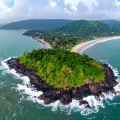 Aerial view of Harihareshwar and Diveagar coastline in Maharashtra, featuring a lush green hill surrounded by the Arabian Sea, curved beach with gentle waves, and a small seaside village nestled along the shore.