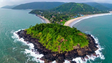 Aerial view of Harihareshwar and Diveagar coastline in Maharashtra, featuring a lush green hill surrounded by the Arabian Sea, curved beach with gentle waves, and a small seaside village nestled along the shore.