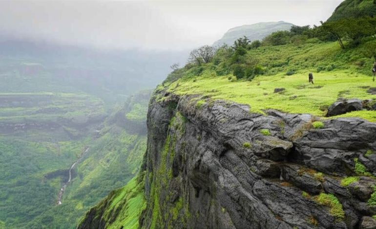 Trekker standing on a lush green cliff edge with panoramic view of the Sahyadri mountain range and valley below during monsoon.