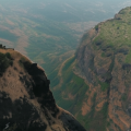 Scenic aerial view of two rocky cliffs at Kavnai Fort in Igatpuri, Maharashtra with a lone trekker and a small temple structure on the hilltop
