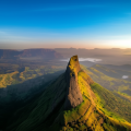 Aerial view of Nhavigad Fort with steep cliffs and lush green valleys under a clear blue and golden sky.