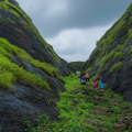 Trekker group climbing stone steps through lush green rock passage at Hadsar Fort in monsoon, Junnar Maharashtra