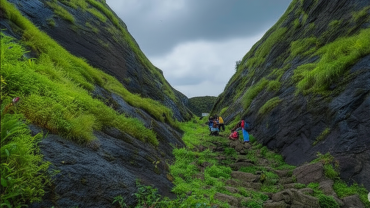 Trekker group climbing stone steps through lush green rock passage at Hadsar Fort in monsoon, Junnar Maharashtra
