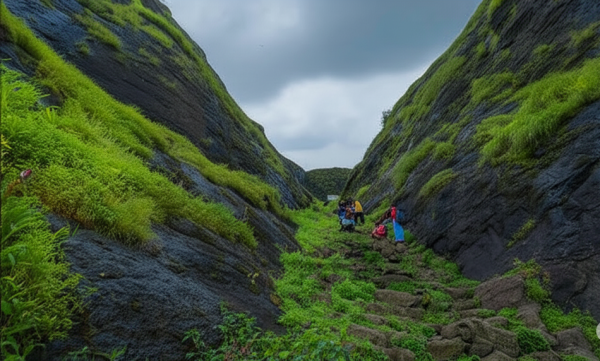 Trekker group climbing stone steps through lush green rock passage at Hadsar Fort in monsoon, Junnar Maharashtra