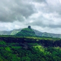 Scenic view of Kothaligad Fort surrounded by lush green hills under a cloudy sky.