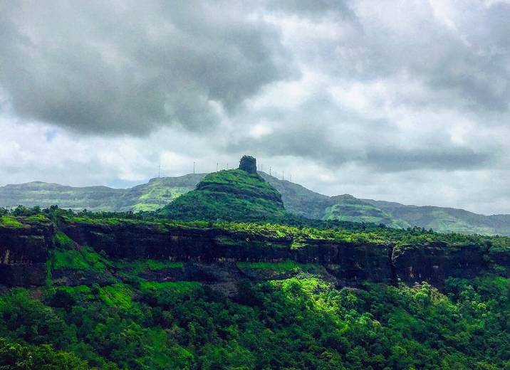 Scenic view of Kothaligad Fort surrounded by lush green hills under a cloudy sky.