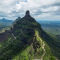 Aerial view of Mangi Tungi twin peaks with a winding path and lush green Sahyadri mountains under a cloudy sky.