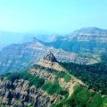 A panoramic view of Vasota Fort surrounded by dense green forest and rugged mountain ridges under a clear blue sky.