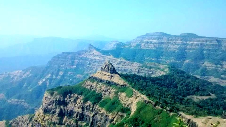 A panoramic view of Vasota Fort surrounded by dense green forest and rugged mountain ridges under a clear blue sky.